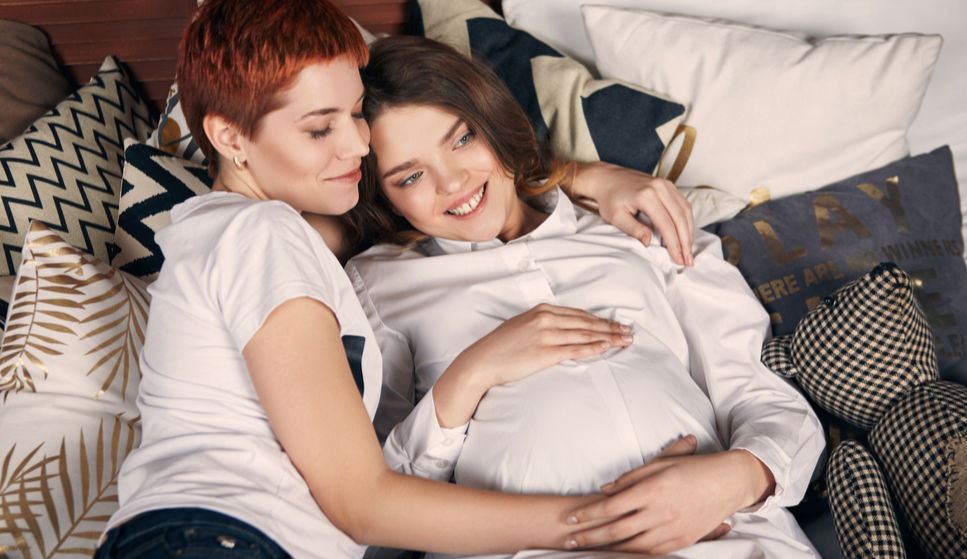 Pregnant lesbian couple hugging on beach stockphoto