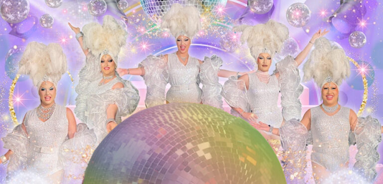 Five drag queens dressed in white sequinned showgirls costumes with feather headresses stand behind a gigantic rainbow disco ball, with a background of lilac lights and disco balls above and behind them.